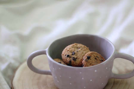 Bowl of chocolate chip cookies and wooden tray on a bed. Selective focus.