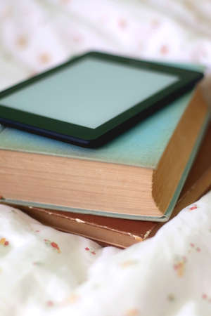 Stack of old hardcover books and digital e-reader on a bed. Selective focus.の写真素材