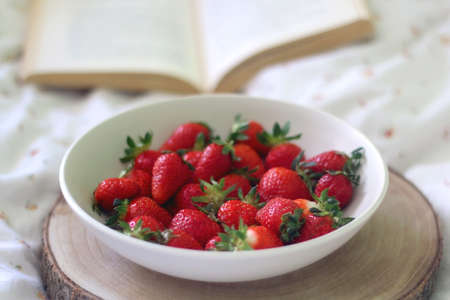 Bowl of strawberries and open book on a bed. Selective focus.の写真素材