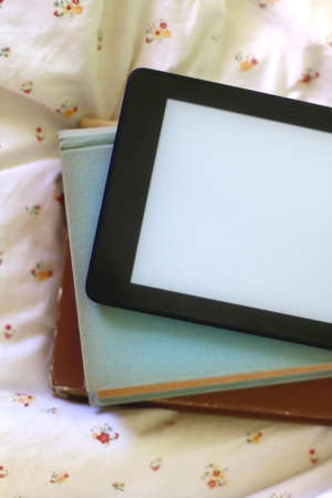 Stack of old hardcover books and digital e-reader on a bed. Flat lay.