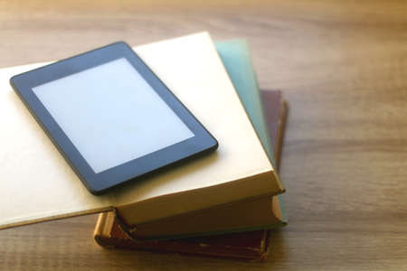 Stack of old hardcover books and e-reader on a table. Selective focus.の写真素材