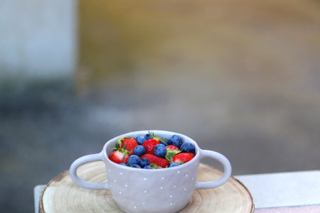 Ceramic bowl with fresh blueberries and strawberries and wooden tray on a table. Selective focus.の写真素材