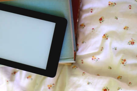 Stack of old hardcover books and digital e-reader on a bed. Flat lay.の写真素材