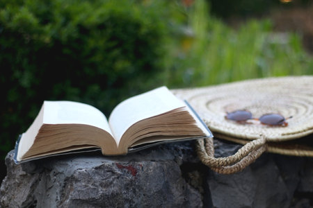 Open book, straw bag and sunglasses in a garden. Selective focus.