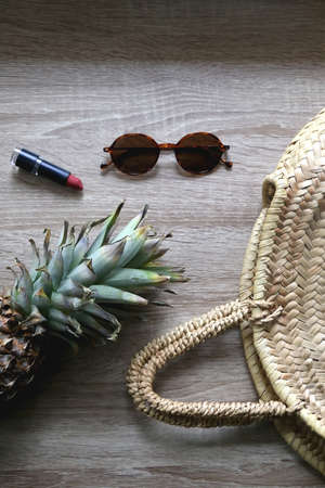 Straw bag, sunglasses, lipstick and pineapple on wooden background. Flat lay.