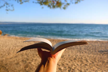 Hand holding open book on a beach. Selective focus.の写真素材
