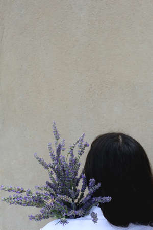Unrecognizable person holding a bouquet of lavender flowers. Selective focus, simple concrete background.の写真素材