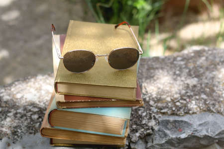 Stack of old vintage books and retro sunglasses in a garden. Selective focus.の写真素材