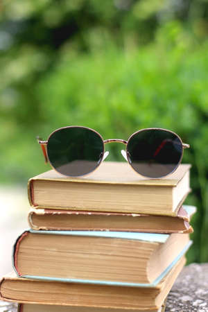 Stack of old vintage books and retro sunglasses in a garden. Selective focus.の写真素材