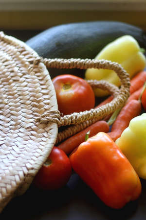 Straw bag filled with various summer vegetables on dark background. Selective focus.の写真素材