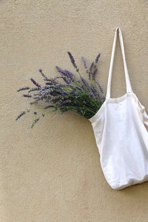 Canvas tote bag filled with fresh lavender flowers, hanging on a concrete wall.