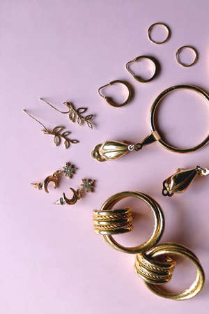 Various gold earrings on pastel pink background. Flat lay.の写真素材