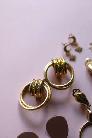 Various gold earrings on pastel pink background. Selective focus.の写真素材