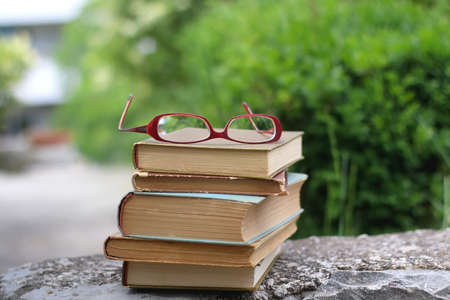 Stack of vintage books and reading glasses in a garden. Selective focus.の写真素材