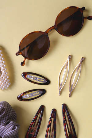 Tortoise shell sunglasses and various hair accessories on yellow background. Flat lay.