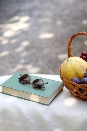 Vintage basket full of various fruit, hardback book and retro sunglasses on picnic basket. Selective focus.の写真素材