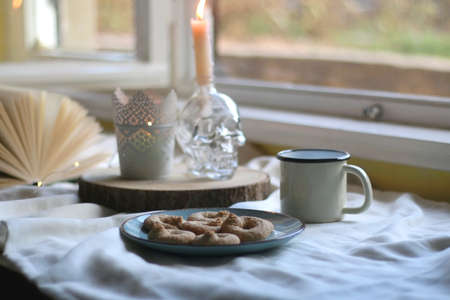 Plate with cookies, open book, lit candles and fairy lights. Hygge at home. Selective focus.の写真素材