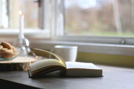 Bowl of cookies, cup of hot beverage, open book and lit candles on a table. Selective focus.の写真素材