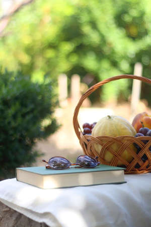 Vintage basket full of various fruit, hardback book and retro sunglasses on picnic basket. Selective focus.の写真素材