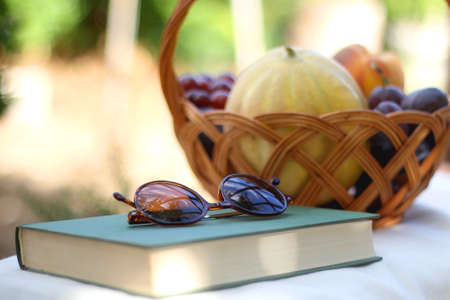 Vintage basket full of various fruit, hardback book and retro sunglasses on picnic basket. Selective...