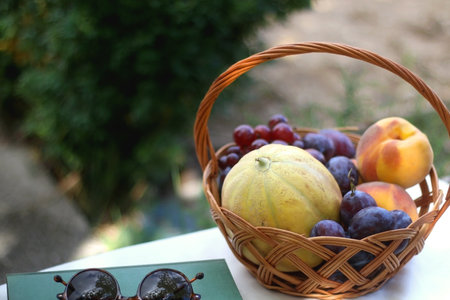 Vintage basket full of various fruit, hardback book and retro sunglasses on picnic basket. Selective focus.の写真素材