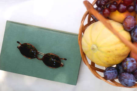 Vintage basket full of various fruit, hardback book and retro sunglasses on picnic basket. Top view.