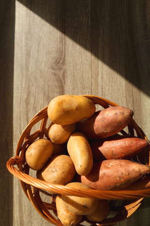Vintage basket filled with potatoes and sweet potatoes on wooden table. Top view.の写真素材