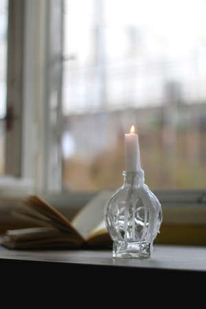 Lit candle in the candle holder and open book on a table. Dark academia concept. Selective focus.の写真素材