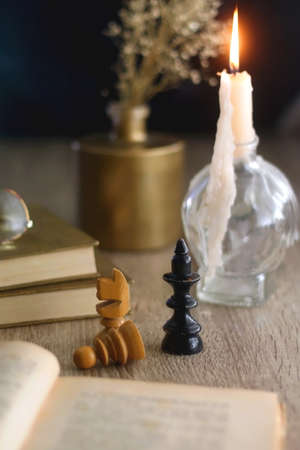 Old books, reading glasses, vintage chess pieces, lit candle and vase with gypsophila flowers. Dark academia concept. Selective focus.の写真素材
