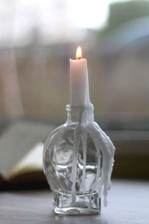 Lit candle in the candle holder and open book on a table. Dark academia concept. Selective focus.
