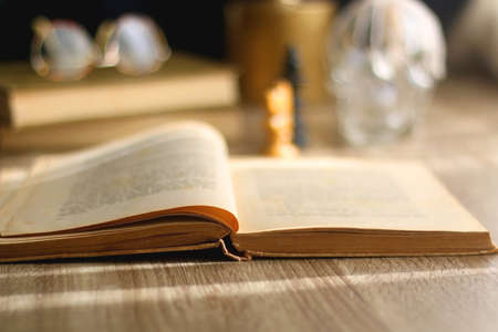 Old books, reading glasses, vintage chess pieces, lit candle and vase with gypsophila flowers. Dark academia concept. Selective focus.の写真素材