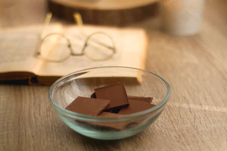 Bowl of chocolate, book, reading glasses, candles and vase with flowers on the table. Selective focus.の写真素材