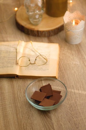 Bowl of chocolate, book, reading glasses, candles and vase with flowers on the table. Selective focus.の写真素材