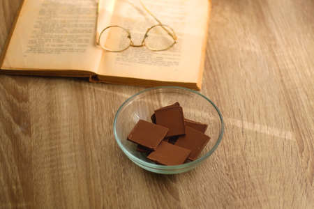 Bowl of chocolate, book, reading glasses, candles and vase with flowers on the table. Selective focus.の写真素材
