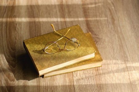 Two vintage hardback books and retro reading glasses on the table. Selective focus.