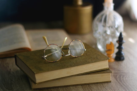 Old books, reading glasses, vintage chess pieces, lit candle and vase with gypsophila flowers. Dark academia concept. Selective focus.の写真素材