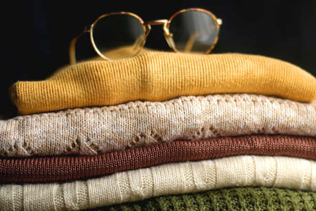 Pile of colorful sweaters in warm tones and eyeglasses with metal frames. Selective focus.の写真素材