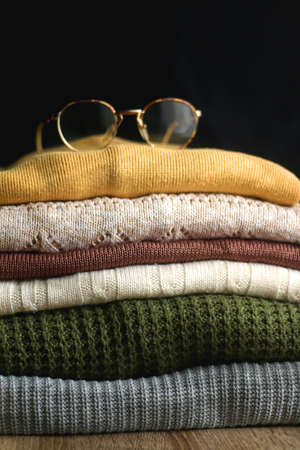 Pile of colorful sweaters in warm tones and eyeglasses with metal frames. Selective focus.の写真素材