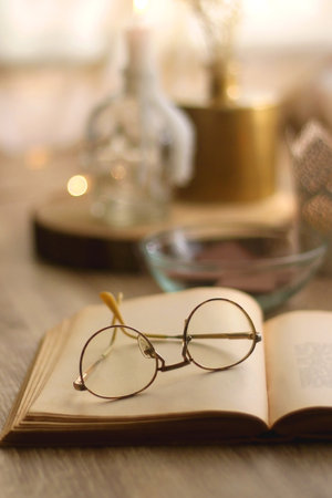 Bowl of chocolate, book, reading glasses, candles and vase with flowers on the table. Selective focus.の写真素材