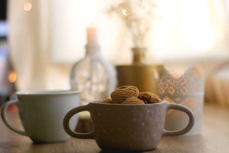 Bowl of cinnamon cookies, lit candles and vase with gypsophila flowers on the table. Selective focus, fairy lights in the background. Hygge at home.の写真素材