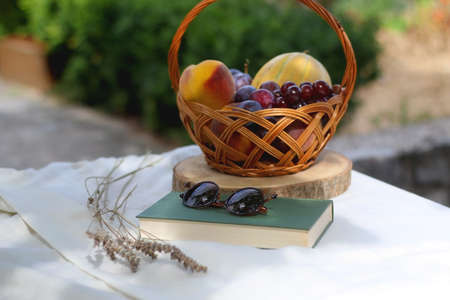 Vintage basket with various fruit, book, sunglasses and lavender flowers on a picnic basket. Selective focus.の写真素材