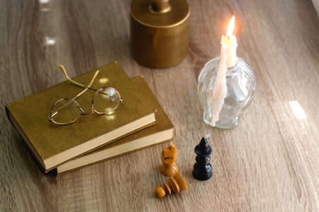 Old books, reading glasses, vintage chess pieces, lit candle and vase with gypsophila flowers. Dark academia concept. Selective focus.の写真素材