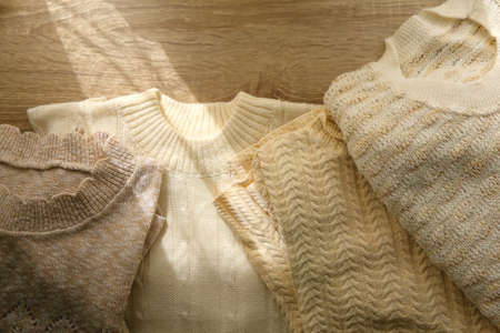 White and beige sweaters on wooden background, illuminated by sunlight. Flat lay.