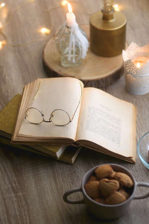 Bowl of cookies, bowl of chocolate, vintage books with reading glasses and lit candles. Hygge at...