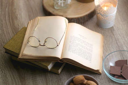 Bowl of cookies, bowl of chocolate, vintage books with reading glasses and lit candles. Hygge at home. Selective focus.の写真素材