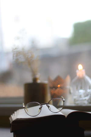 Open book, reading glasses, lit candles and vase with flowers. Hygge at home. Selective focus.の写真素材