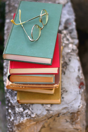 Stack of vintage hardcover books and reading glasses in a garden. Selective focus.の写真素材