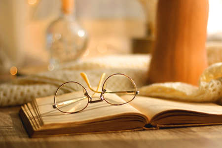 Butternut squash, soft blanket, open book, reading glasses and lit candles. Autumn season, hygge at home. Selective focus.の写真素材