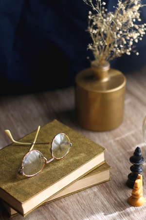 Old books, reading glasses, vintage chess pieces, lit candle and vase with gypsophila flowers. Dark academia concept. Selective focus.の写真素材