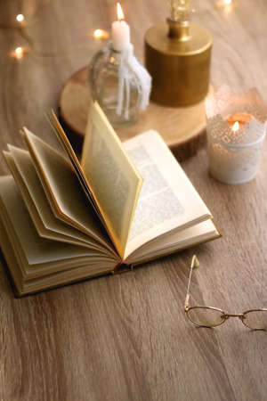Open book, reading glasses, various candles and vase with flowers. Hygge at home. Selective focus.の写真素材